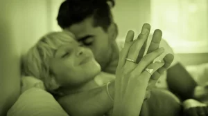 Soft-focus couple cuddling and holding hands in bed, evoking relaxed intimacy.