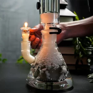 Beaker bong filled with dense white vapor as a lighter heats the bowl; downstem bubbling in clear glass.