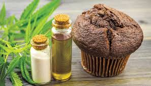CBD oil bottles beside a chocolate muffin and cannabis leaf, showing CBD baking ingredients.